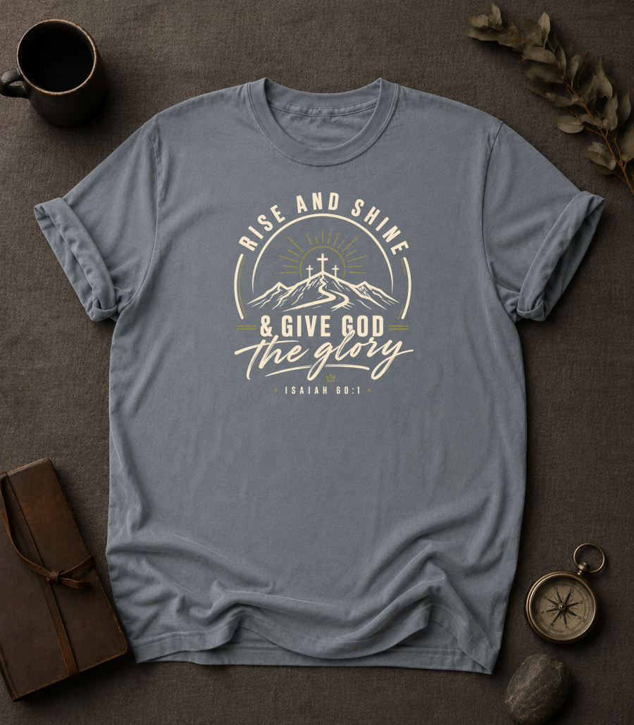 granite Comfort Colors t-shirt with "Rise and Shine & Give God the Glory" Isaiah 60:1 mountain sunrise cross design in Bay colorway, styled with coffee mug, compass, and leather journal