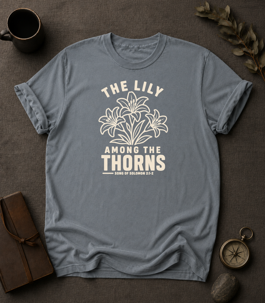 granite Comfort Colors t-shirt with "The Lily Among the Thorns" Song of Solomon 2:1-2 lily flower design in Bay colorway, styled with coffee mug, compass, and leather journal