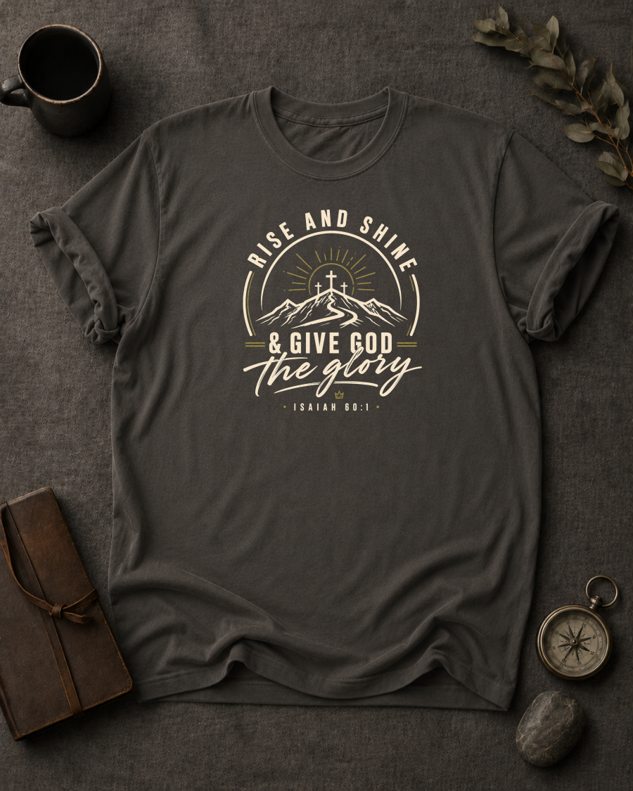 pepper Comfort Colors t-shirt with "Rise and Shine & Give God the Glory" Isaiah 60:1 mountain sunrise cross design in Bay colorway, styled with coffee mug, compass, and leather journal


